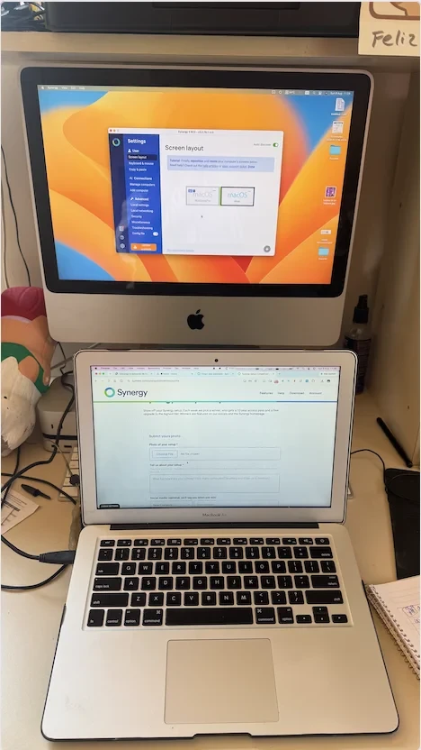 Two Macs separated by six years, connected by Synergy so one keyboard and trackpad reach both. The 2009 iMac and 2015 MacBook Air run side by side, with the screen layout configured to keep cursor movement between them natural.