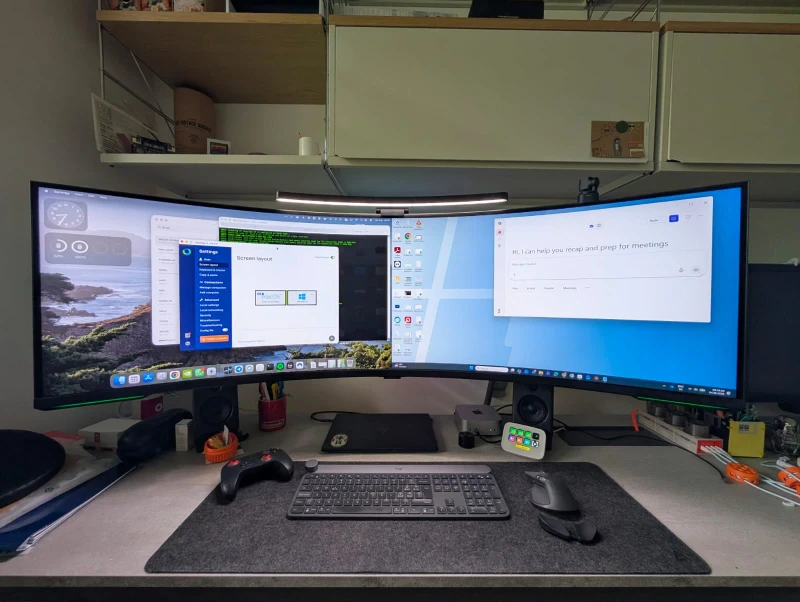 macOS on the left, Windows 11 on the right, both controlled by one keyboard and mouse sliding across a single 57-inch curved panel. Synergy handles the handoff between the Mac Mini M4 and the ARM laptop without any input switching.