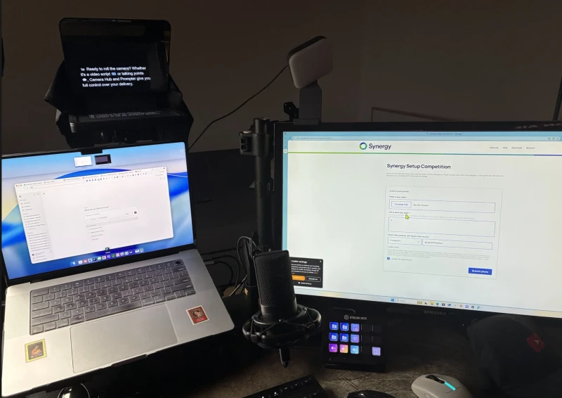 Built around video recording, this desk pairs a Mac laptop with a Windows PC and a teleprompter for scripted shoots. Synergy lets one keyboard and mouse serve both machines, so editing, scripting, and recording prep can move between them without switching inputs.