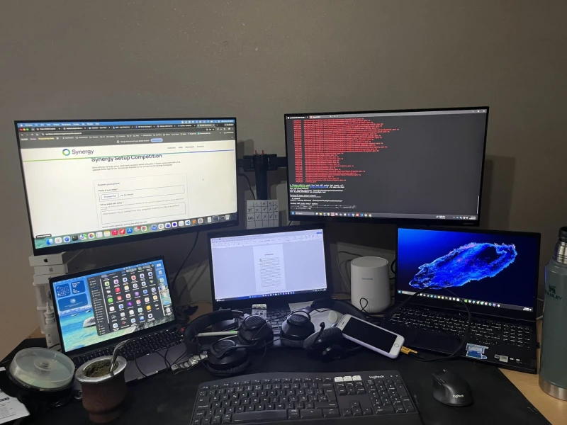 Three laptops running side by side, two of them extended onto their own external monitors, all controlled with one keyboard and mouse through Synergy. One set of peripherals covering that many machines means no switching between inputs regardless of which screen needs attention.