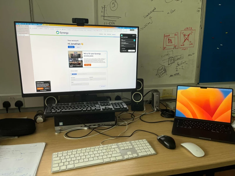 The goal here is cutting desk clutter while working across a Windows desktop and MacBook Pro. Rather than switching the keyboard and mouse physically, Synergy handles input sharing so one set covers both machines, with the monitor's input source toggling between them as needed.