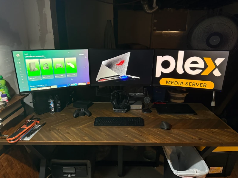 Being an over-the-road truck driver shapes every choice here. The ASUS ROG laptop and a console pack up at a moment's notice for life on the road, while the GEEKOM mini PC stays home running Plex. Back at the handbuilt 6-foot desk, all three screens come together for gaming and media on demand.