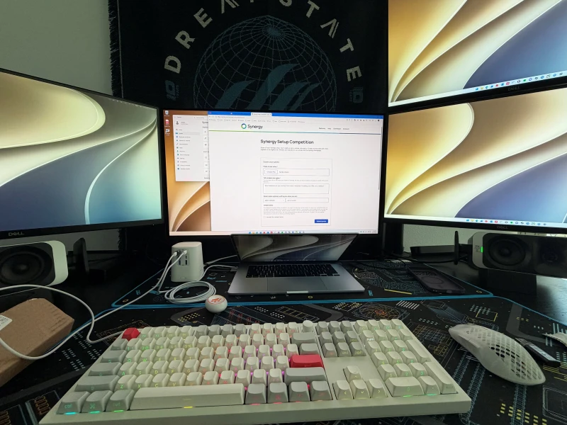 Gaming, computer science projects, and DJing all happen at this desk, split across a Windows desktop and two MacBook Airs. Synergy connects all three so the same keyboard and mouse reach whichever machine is needed, with the cursor moving between them fast enough that being on WiFi rarely matters.