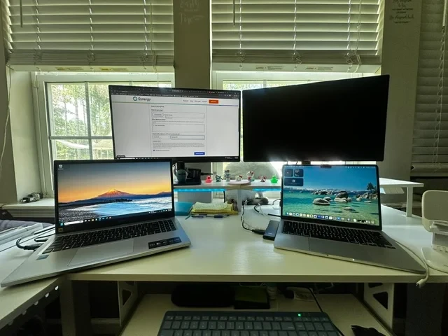 One Mac and one Windows laptop share a single keyboard and mouse here, kept in sync through Synergy across both platforms. Simple setup, practical result.