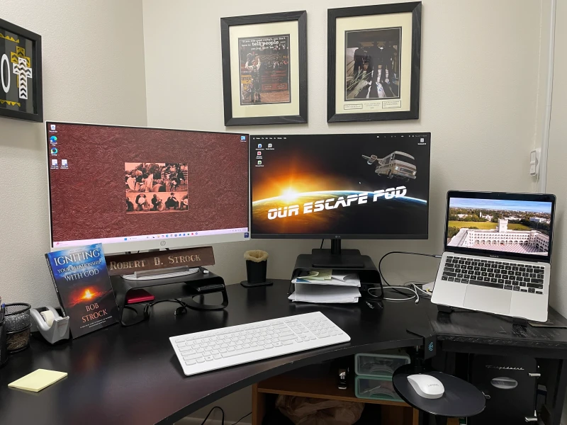 The center monitor's "Our Escape Pod" wallpaper hints at a personal project running on the MacBook, while Synergy ties the Mac and HP together so one Lenovo mouse and keyboard reach both without swapping. An Insignia splitter and a stand with a built-in splitter keep the cabling tidy.