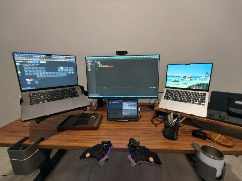 Synergy connects a MacBook Pro M1 Max on the left to a MacBook Air M4 on the right, with the center monitor and tablet both extending the Air. One split keyboard moves input across both Macs without any manual switching.