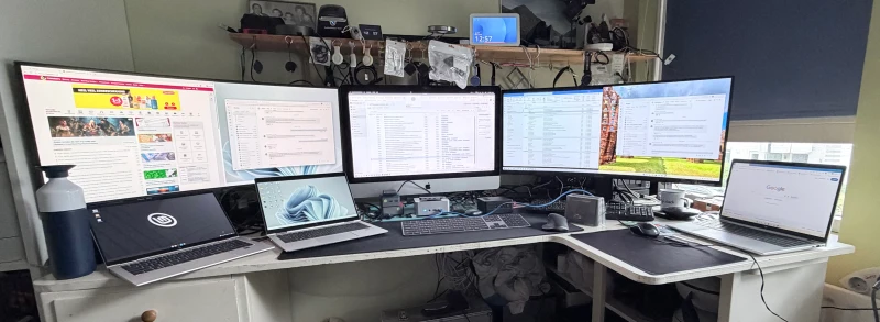 Five machines across three operating systems, all controlled with a single Satechi keyboard and MX Master 3s. The iMac sits at the center, flanked by a Minisforum i9 NUC, two HP Elitebooks on Windows 11, and a Linux Mint notebook, each with its own extended display.