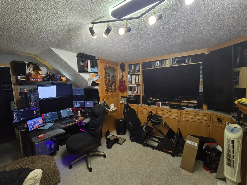 The racing sim setup here pulls double duty: while others are racing, the desk machine handles race configuration for the next session, all through Synergy. The main PC pairs an RTX 5080 with a 9950X3D, joined by two gaming laptops, an X1 Carbon, and a Steam Deck on the same input.