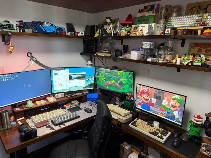 Four machines, one keyboard and mouse: a 10900K with an RTX 5080, a Mac mini M4, a 5600X build, and a 9700X compact card system all share the same inputs through Synergy. The shelves packed with figures, LEGO, and collectibles make the space feel lived-in between sessions.
