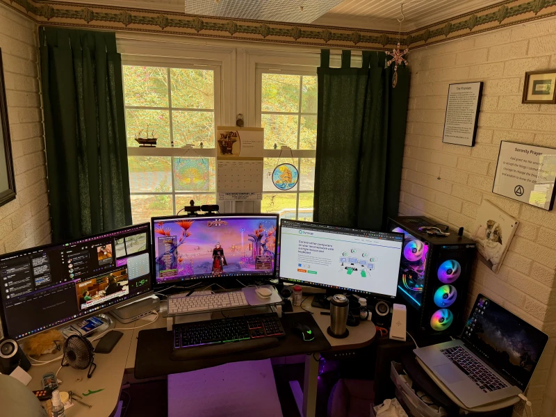 One keyboard and mouse covers three machines here: a Mac Mini M2 on the left, a Windows PC driving the two center displays, and an older MacBook Pro on the right. Gaming, browsing, and whatever else is running all stay reachable without touching a second input device.
