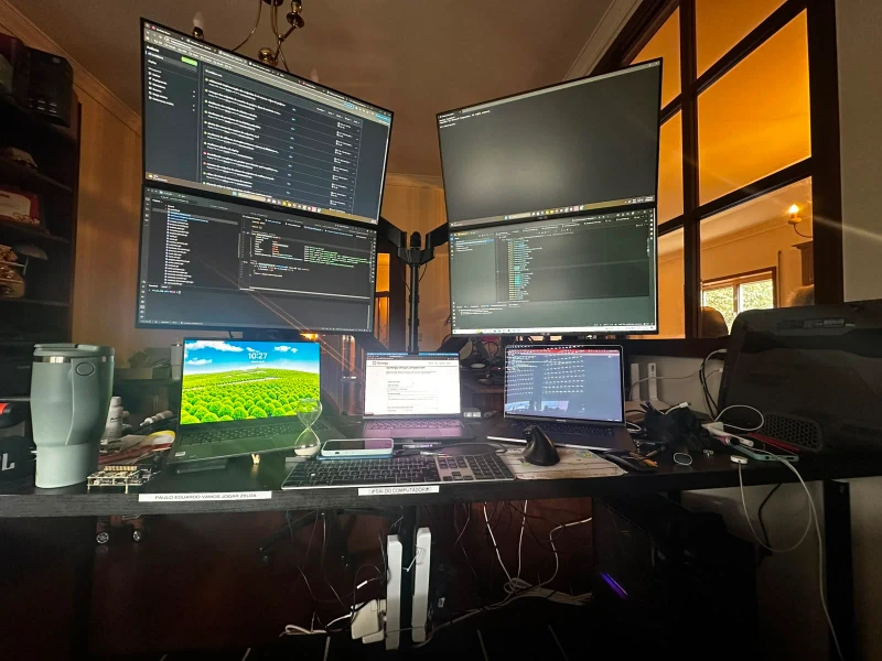 Four machines share this desk, two Macs and two ROG builds, with one keyboard and mouse moving between all of them through Synergy. The handwritten notes taped to the desk edge are a personal touch that no software can replicate.